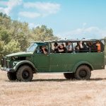 A green tourist jeep with a group of people traveling outdoors.