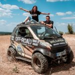 автомобил оф-роуд със състезателна графика и двама души на покрива.