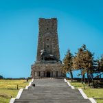 Висока кула с статуя на Лъв, исторически символ на България, на фона на ясно синьо небе.