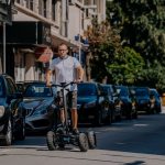 Улица в България, мъж кара електрически скутер, градски пейзаж, съвременен начин на придвижване.